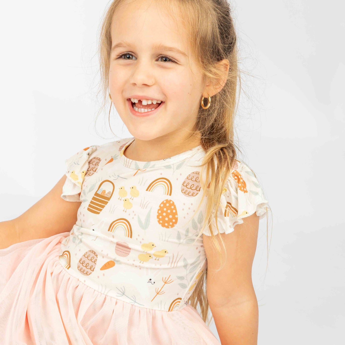 Little girl smiling in her tulle bamboo dress. She is wear the print hop to it that features an easter egg, chicks, bunnies and more!