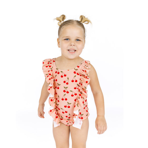 Young girl wearing a pink swimsuit with cherry pattern on a white background