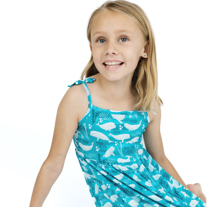 Young girl wearing a blue dress with white whale patterns on a white background