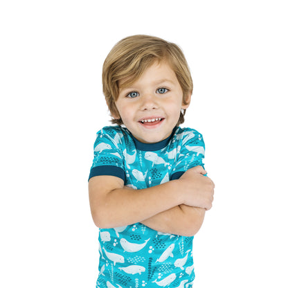 Child wearing a blue shirt with whale pattern on a white background