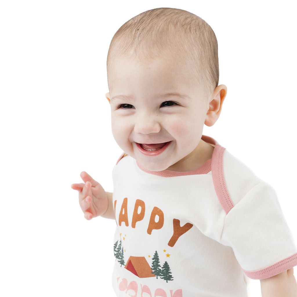 A smiling baby wearing a white short-sleeve t-shirt with pink trim and a 'HAPPY CREEP' graphic, paired with light blue denim jeans, set against a plain white background.