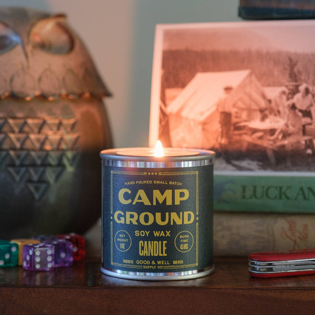 Camp Ground candle in a tin with a vintage photo and decorative items in the background