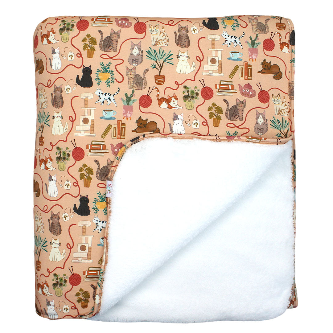 fleece lined bamboo blanket featuring cats, yarn plants, tea and cat toys on an orange hue color.  