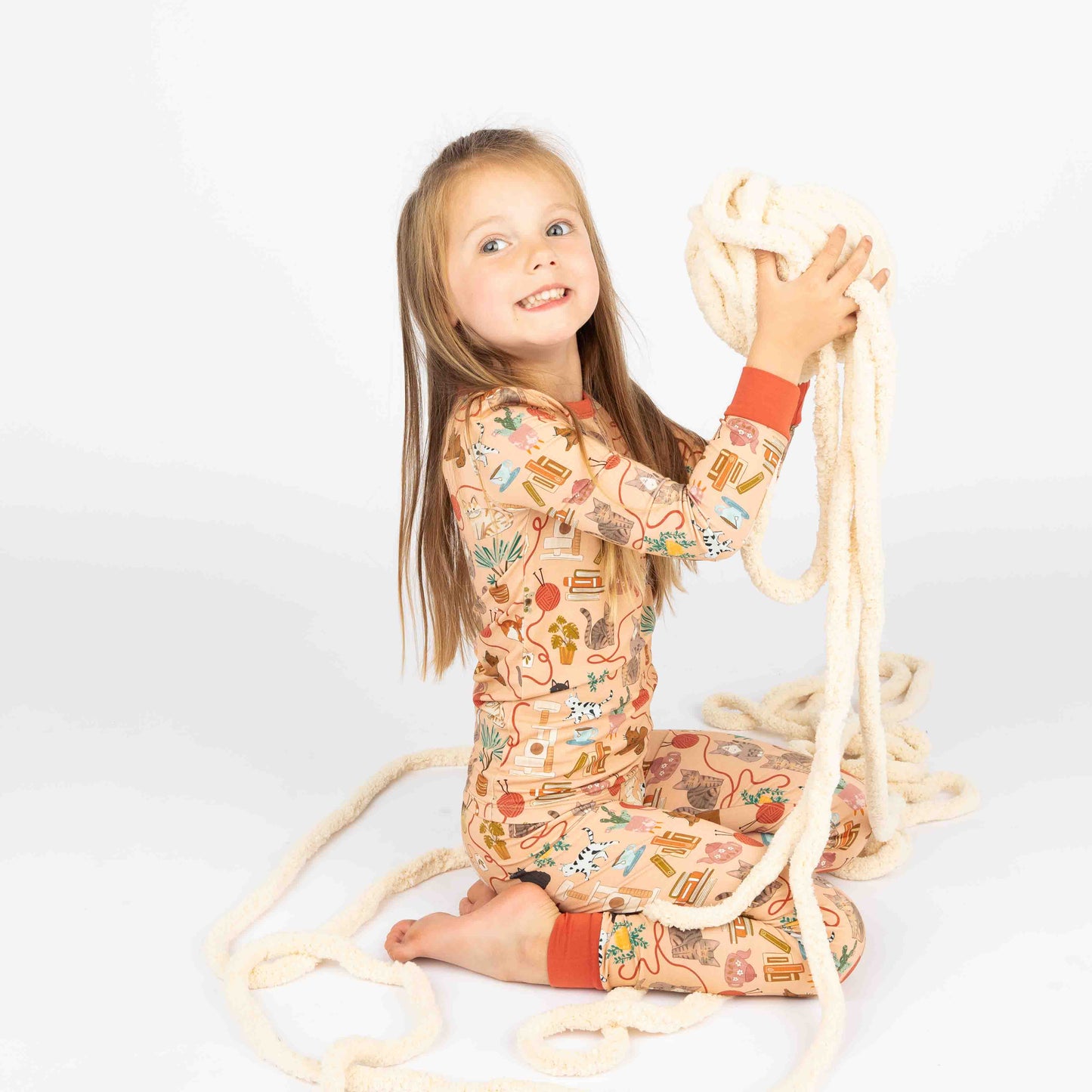 Young girl holding ball of yarn modeling bamboo pajama long-sleev set. The print featured is our cat print