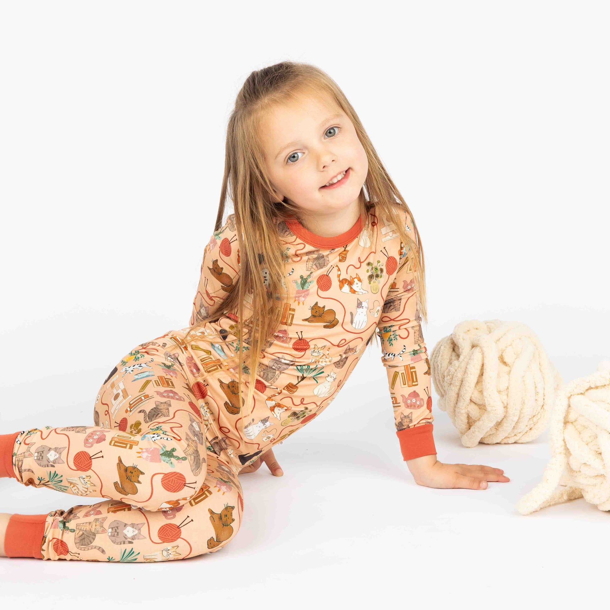 Young girl holding ball of yarn modeling bamboo pajama long-sleeve set. The print featured is our orange hue cat print