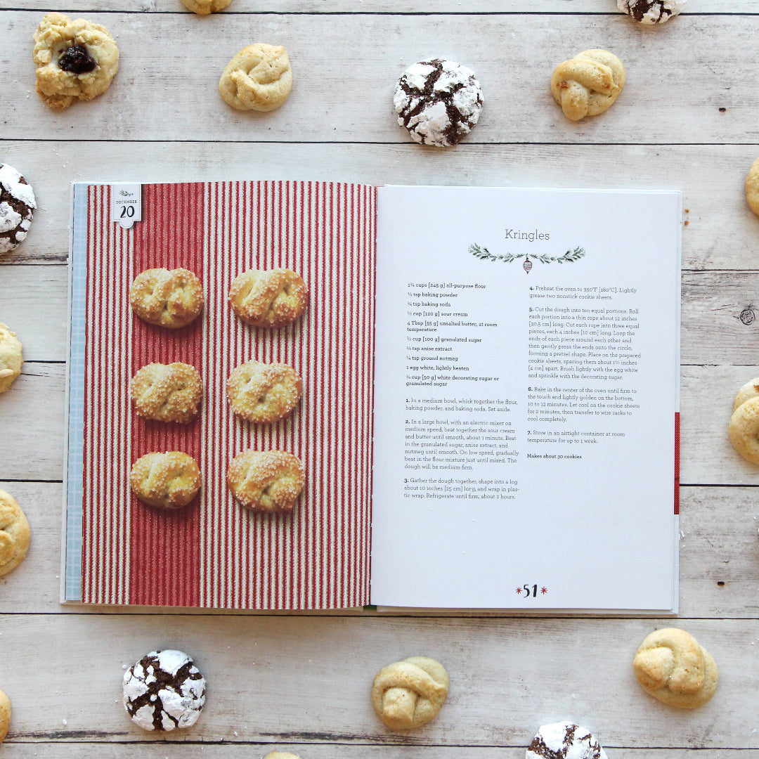 Cookbook open to a page with cookie recipes surrounded by various cookies on a wooden surface