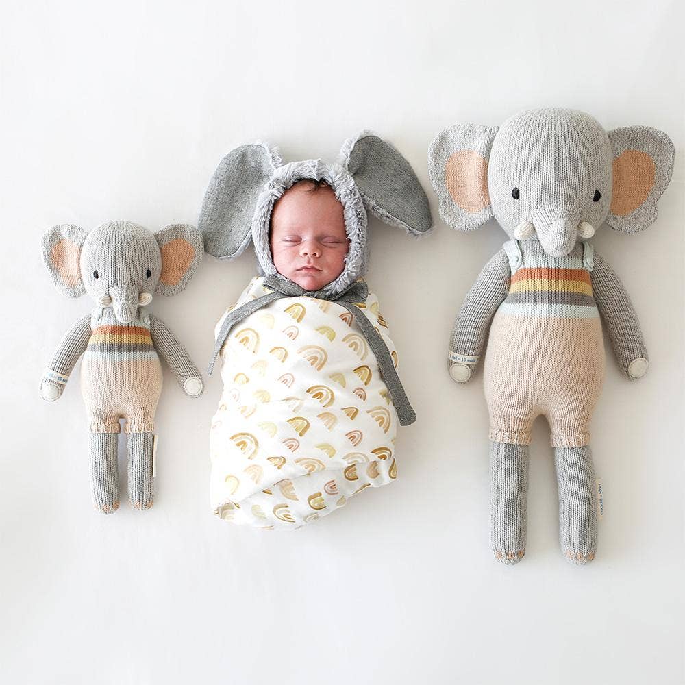 Baby in an elephant costume surrounded by two elephant plush toys on a white background
