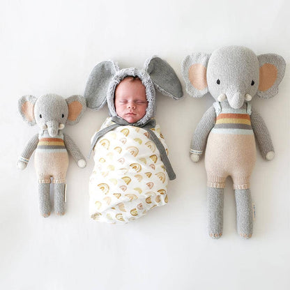 Baby in an elephant costume surrounded by two elephant plush toys on a white background