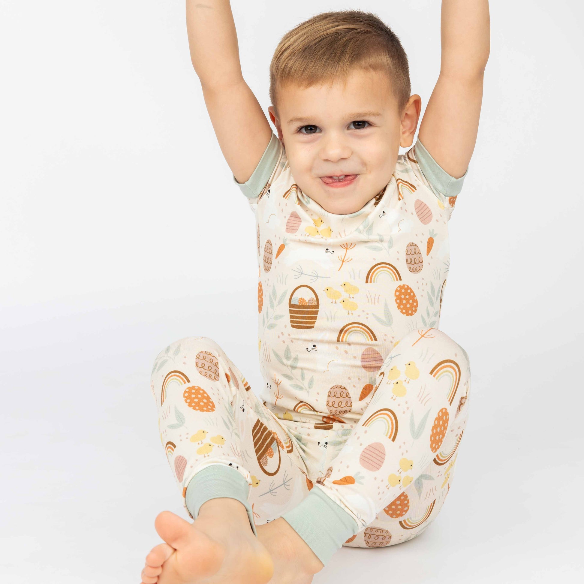 Little boy sitting down with his hands up with a playful face in our hop to it print that features bunnies, chicks, easter eggs and more!