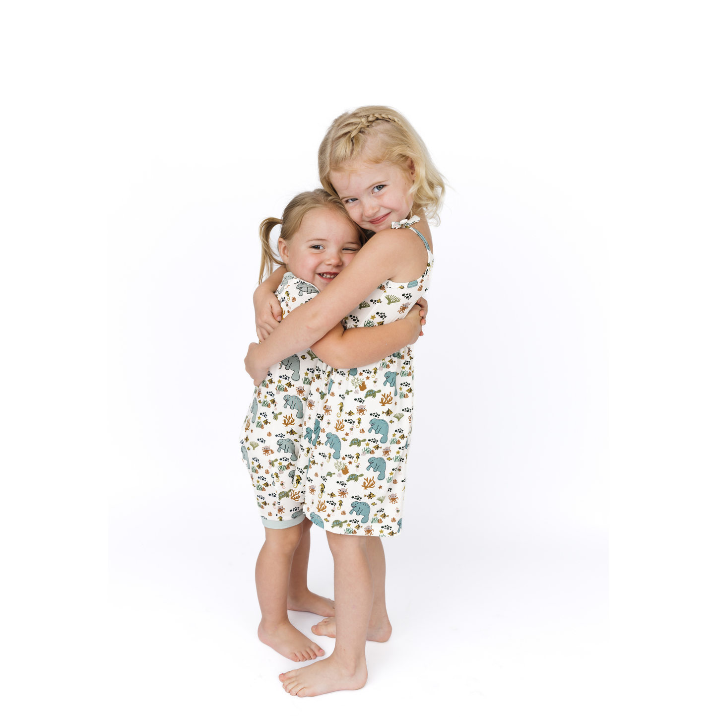 Two children wearing matching manatee-patterned pajamas on a white background
