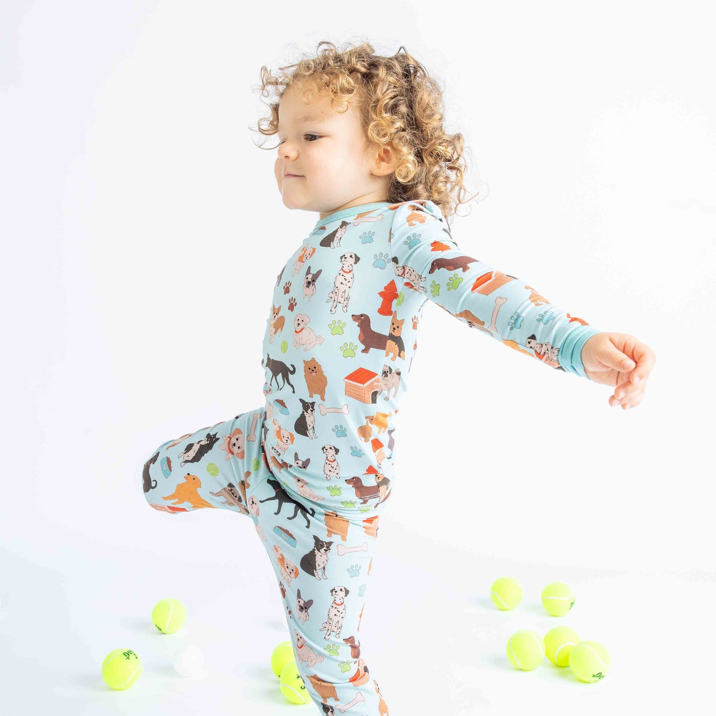 Kid dancing with tennis balls behind him while modeling the "dogs Bark" Print that is blue featuring different types of dogs, a dog house, paw prints, bones, and more!