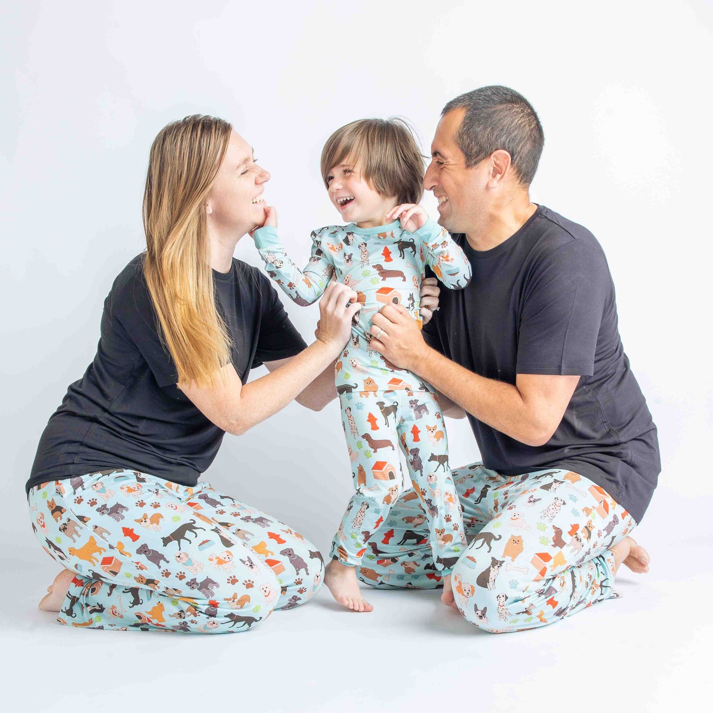 Mom, Dad, and son laighing and modeling the "dogs Bark"   Print that is blue featuring different types of dogs, a dog house, paw prints, bones, and more!