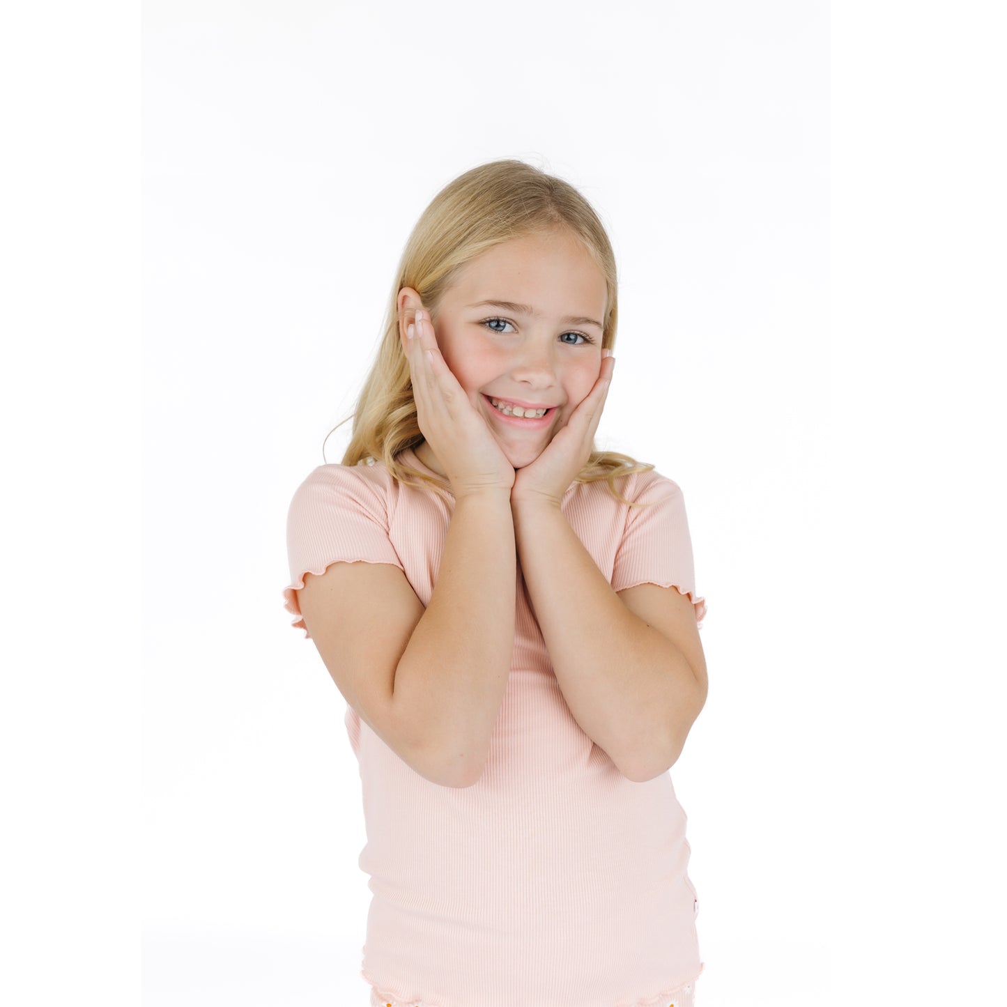 Young girl in a pink shirt posing with hands on face against a white background