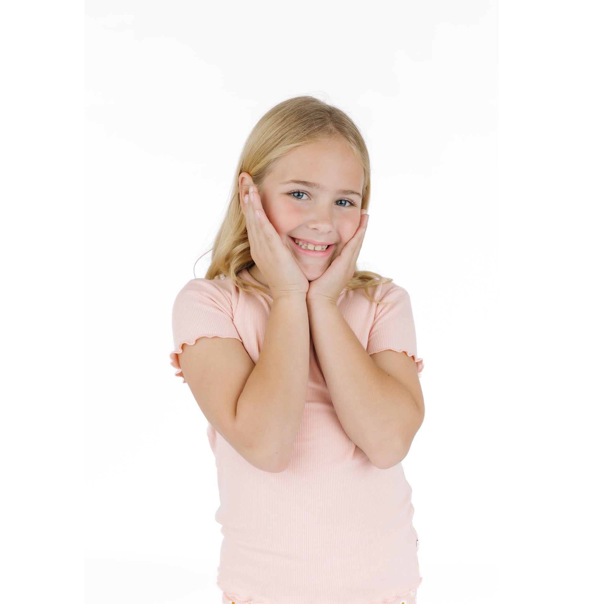 Young girl in a pink shirt posing with hands on face against a white background