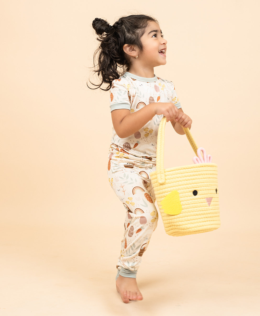 Little girl smiling with her chicks easter basket in our hop to it two piece bamboo pajama that features eggs, chicks, bunnies and more!