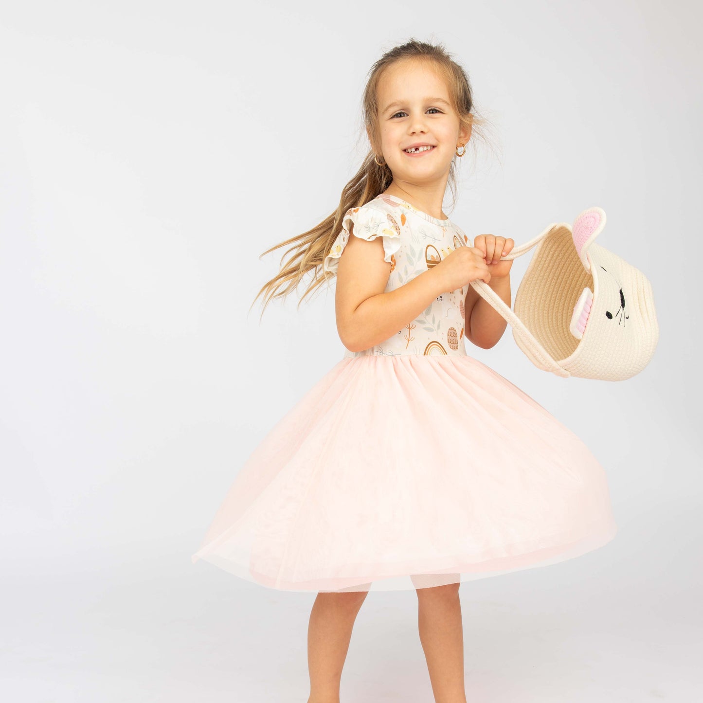 Little girl holding a white bunny easter basket. She has on our tulle bamboo dress that features easter eggs, bunnies, chicks and more!