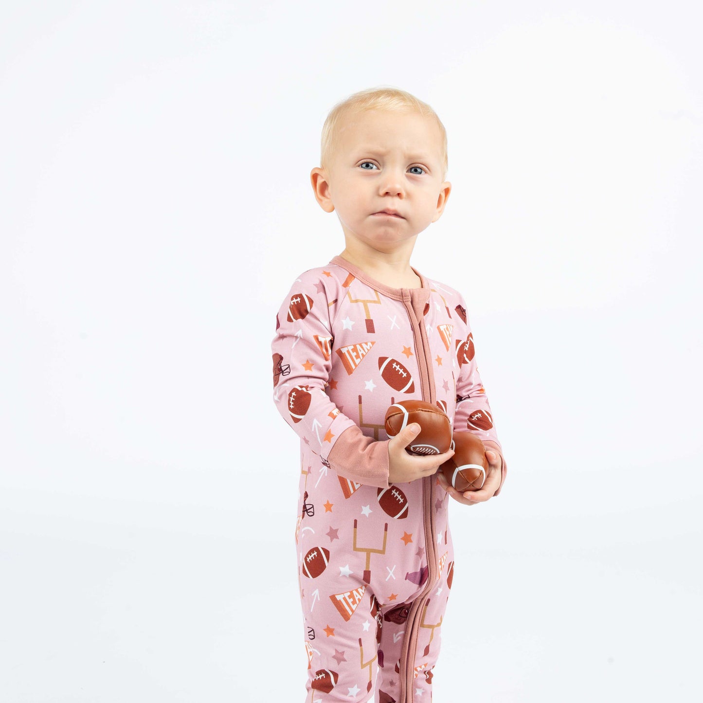 Girl standing with footballs in each hand wearing our pink football print called "Game Day" Featuring footballs, goal posts, stars and more! 