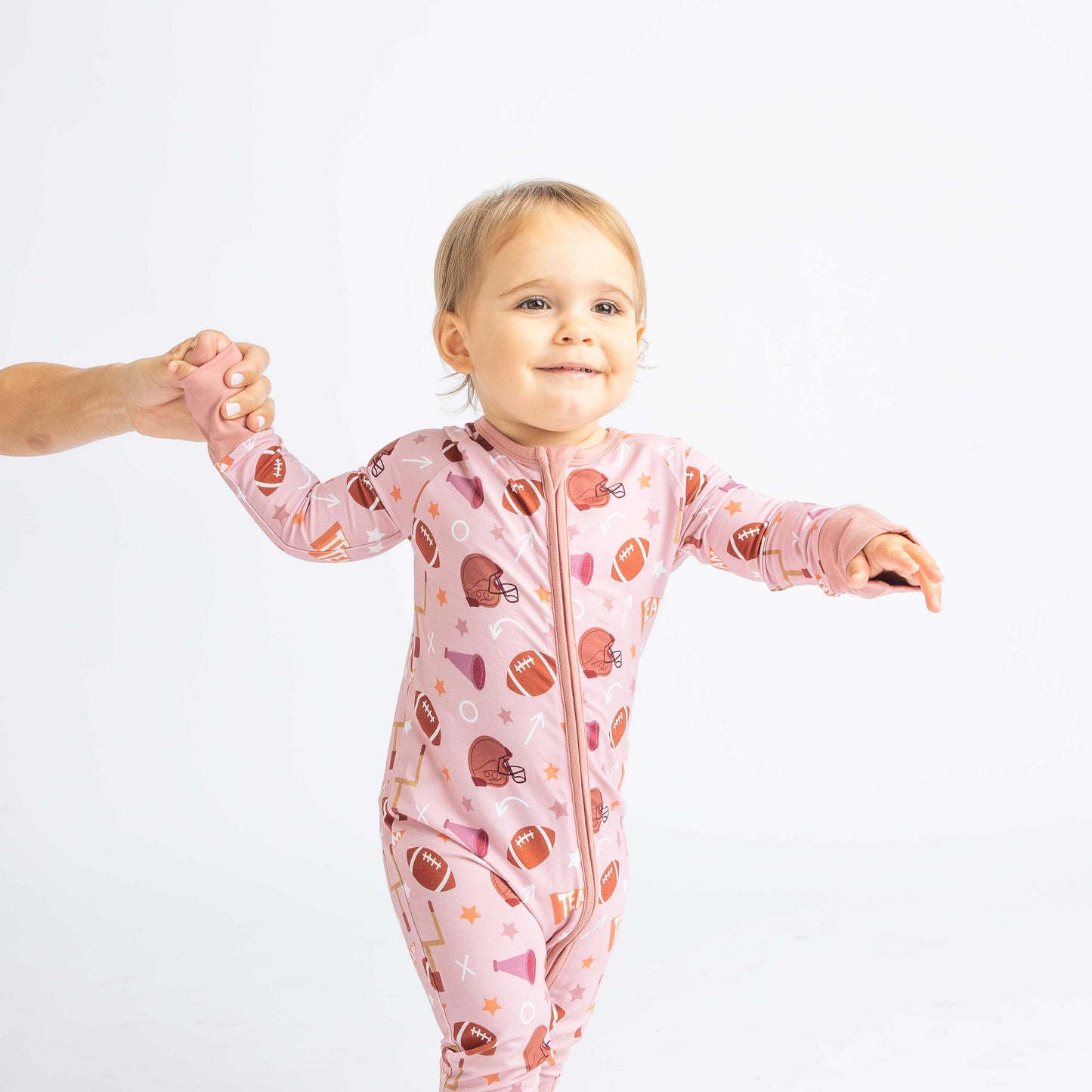 Girl smiling and walking while modeling our pink football print called "Game Day" Featuring footballs, goal posts, stars and more! 