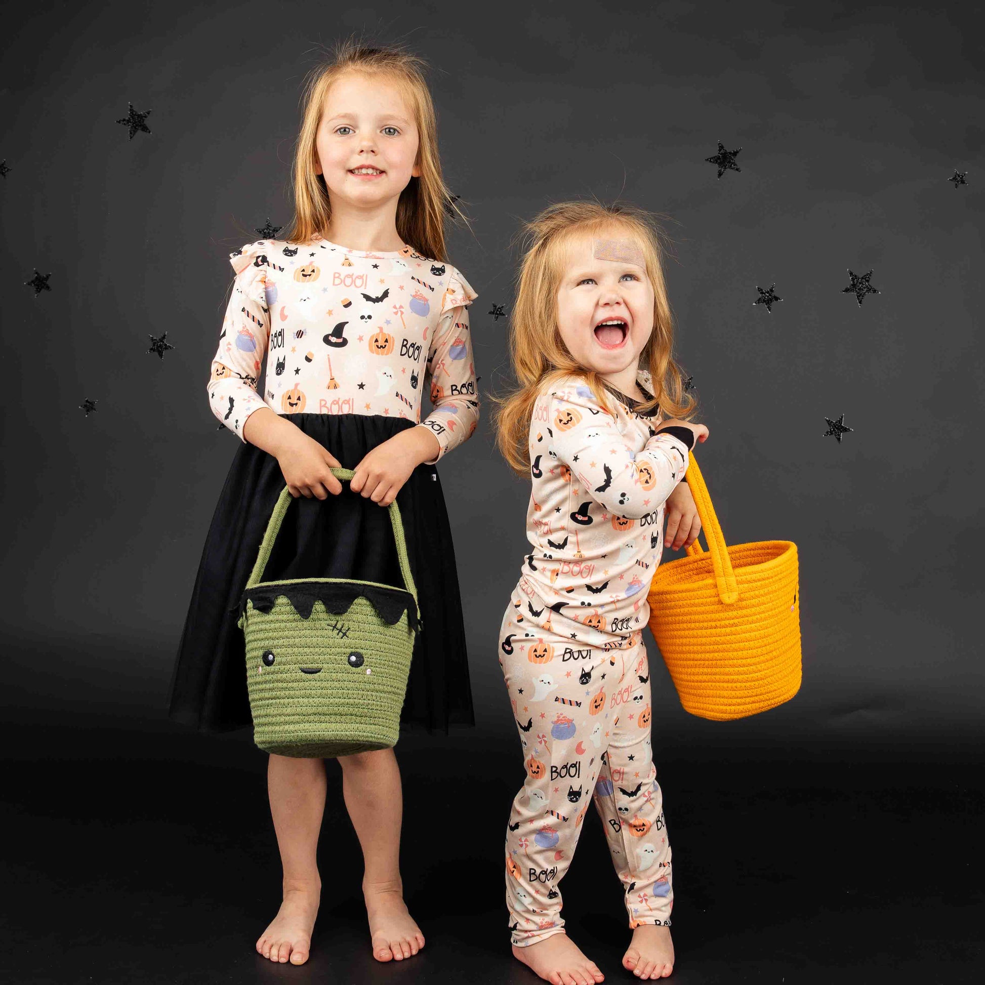 2 girls standing and smiling at camera while wearing pink halloween clothes and holding the pumpkin rope basket and the Frankenstein rope basket