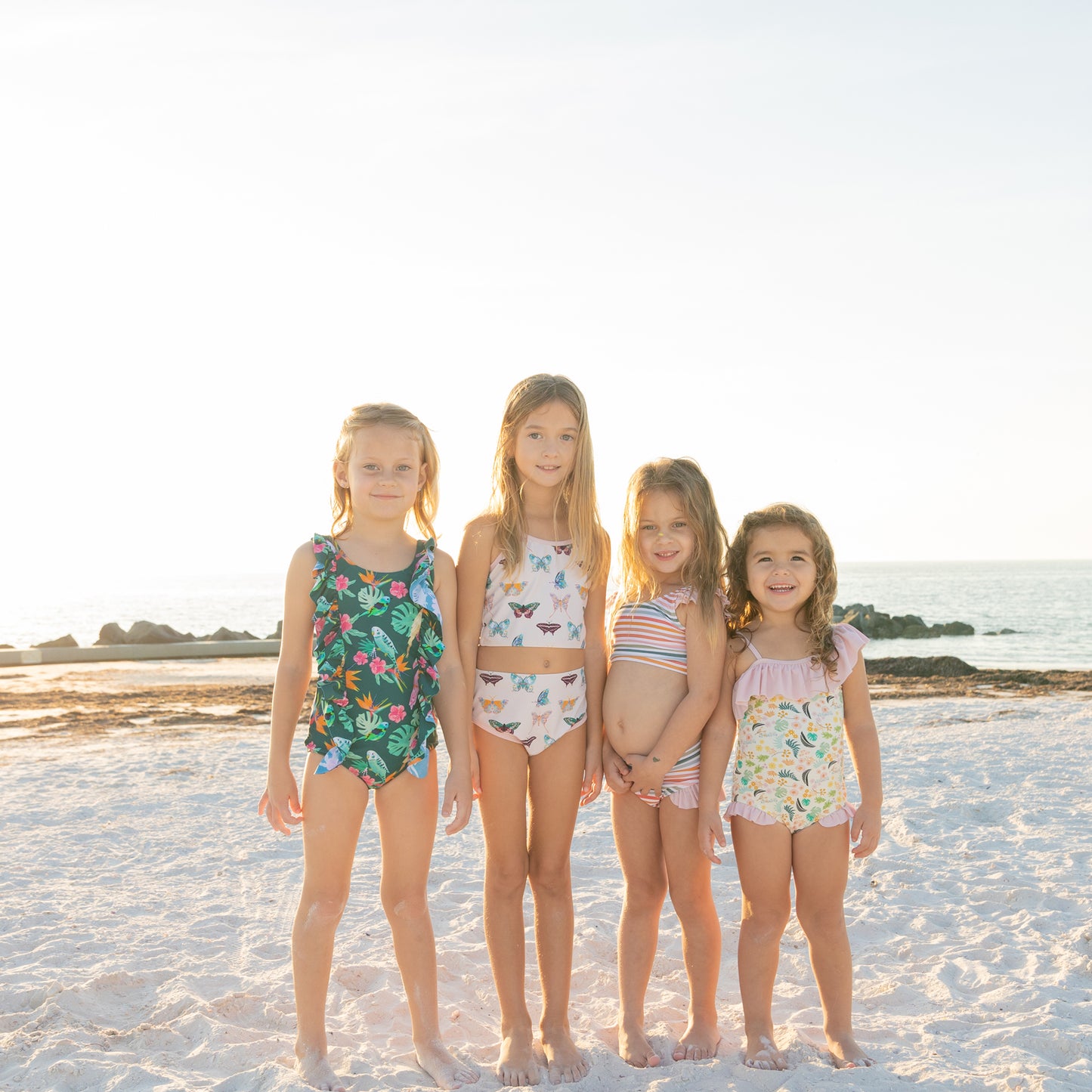Four young girls standing on a sandy beach wearing colorful swimsuits.
