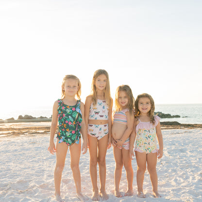 Four young girls standing on a sandy beach wearing colorful swimsuits.