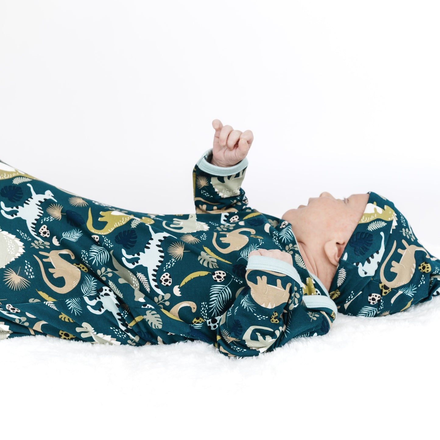 Baby lying on a white surface wearing a dinosaur-patterned onesie.