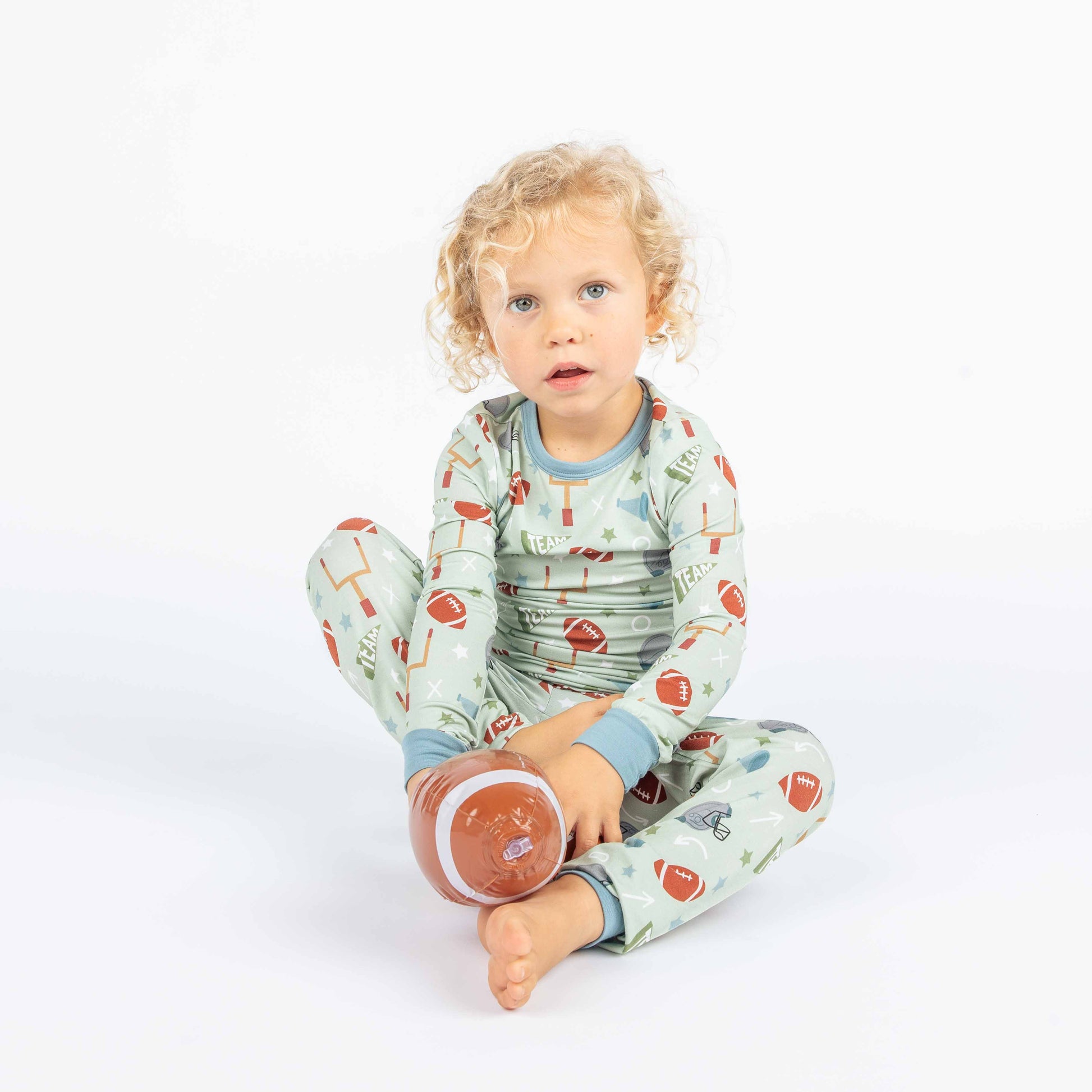 Kid sitting with football in his hand modeling our green football print called "Game Day" Featuring footballs, goal posts, stars and more!