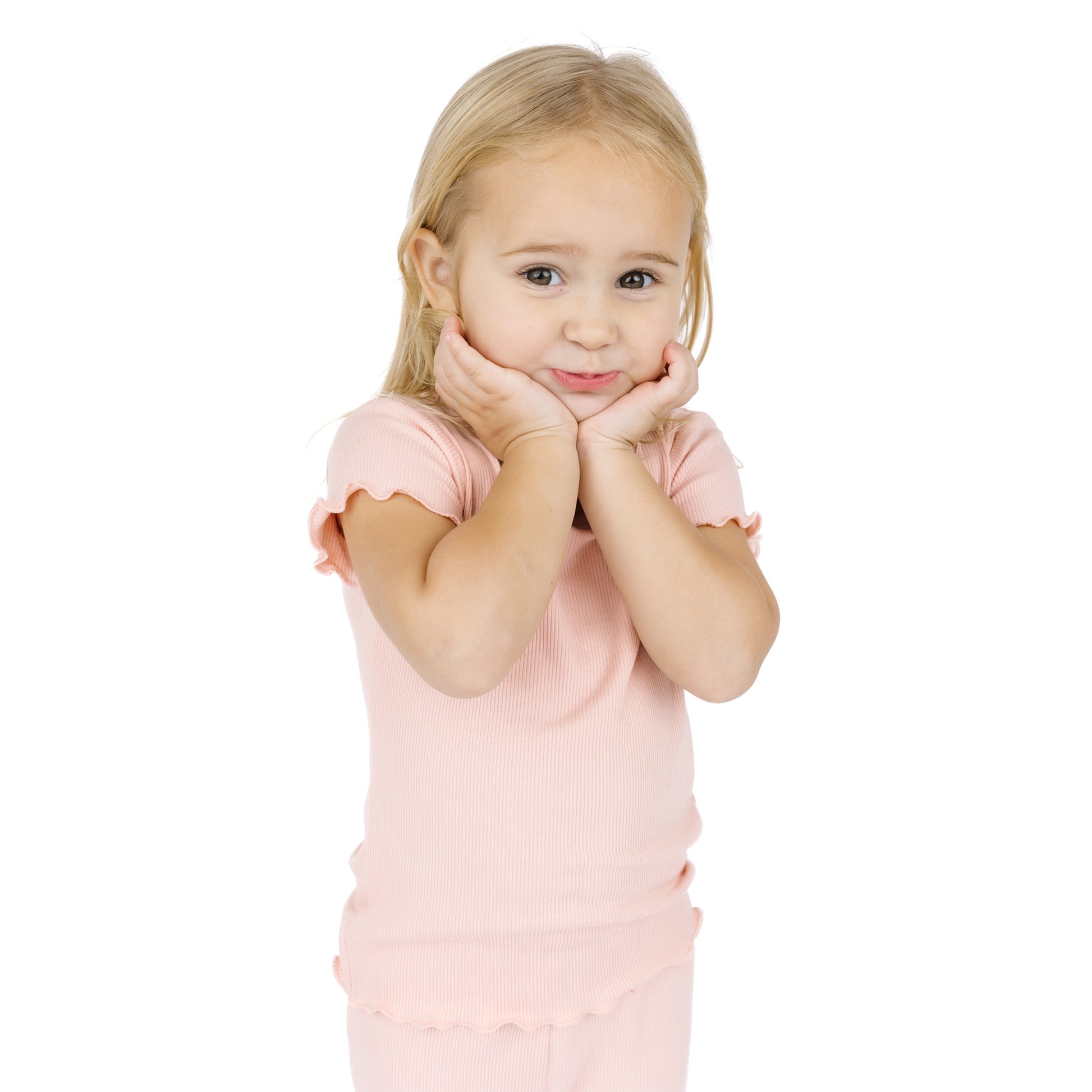 Young girl in a pink dress posing with hands on chin against a white background