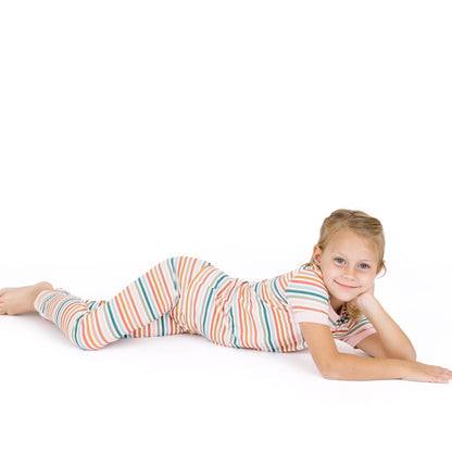 Young girl lying on a white surface wearing a colorful striped outfit.