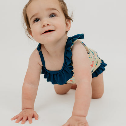 Baby girl crawling in a white background wearing our Emerson and Friends Coral Reef Ruffle Leg One Piece Girls Swimsuit, featuring a vibrant ocean-inspired print with sharks, sea turtles, and coral, designed with adorable ruffle accents and a secure fit for fun beach and pool days.