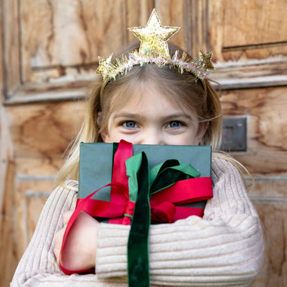 Child wearing a festive outfit with the glittery gold star headband, holding a wrapped gift from Great Pretenders