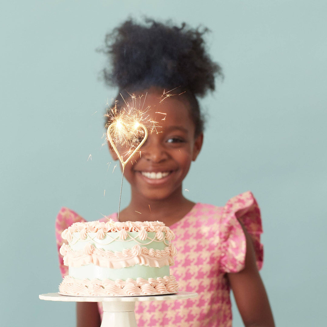 Young girl holding a cake with a sparkler, against a light blue background
