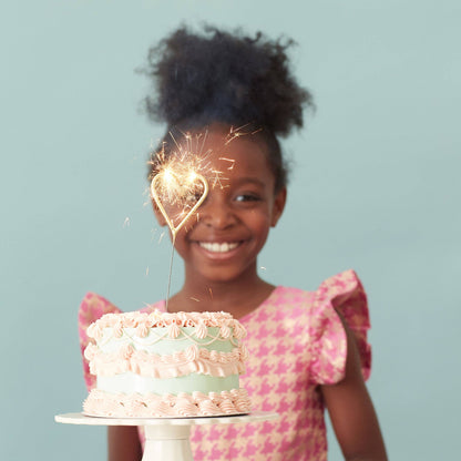 Young girl holding a cake with a sparkler, against a light blue background