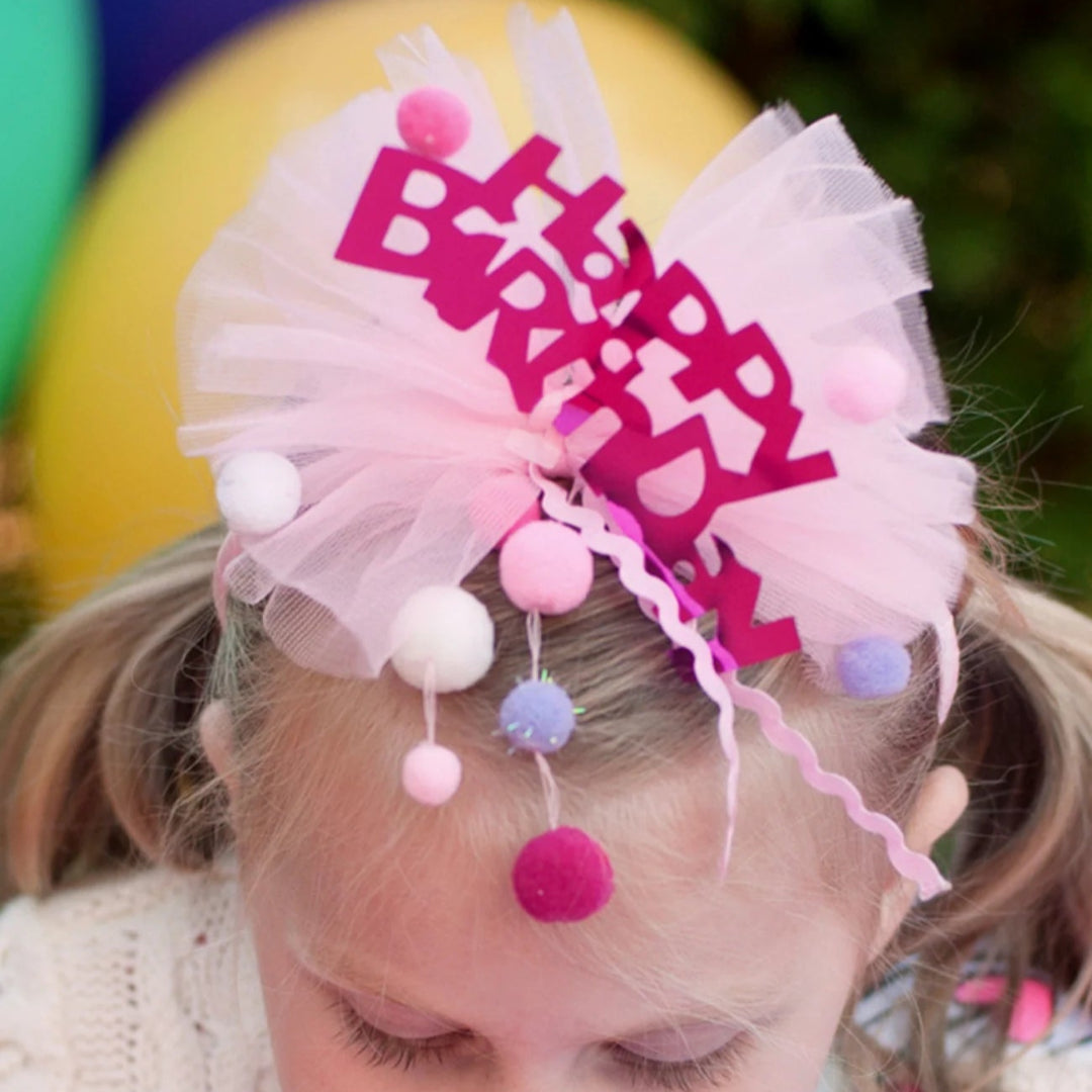 Young girl blowing out candles on a birthday cake with the Happy Birthday  headband on her head