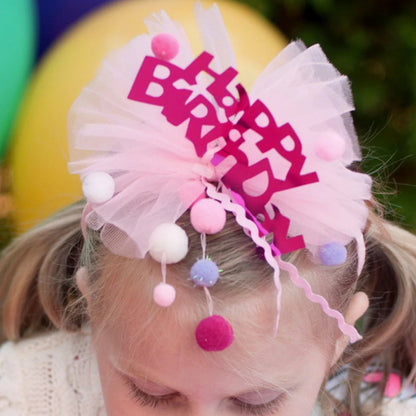 Young girl blowing out candles on a birthday cake with the Happy Birthday  headband on her head