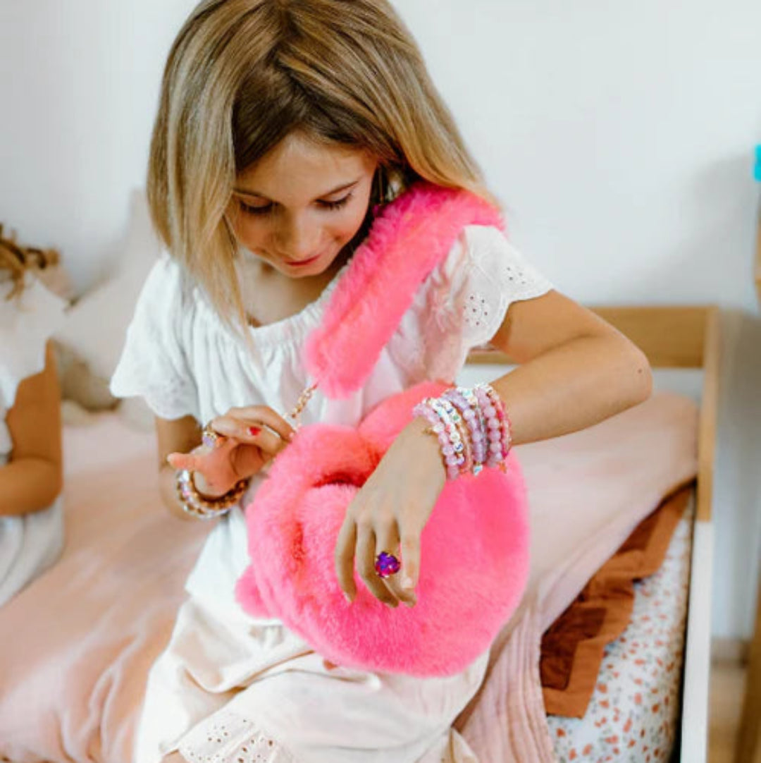 Young girl sitting on a bed putting items into her pink fuzzy purse from Great Pretenders