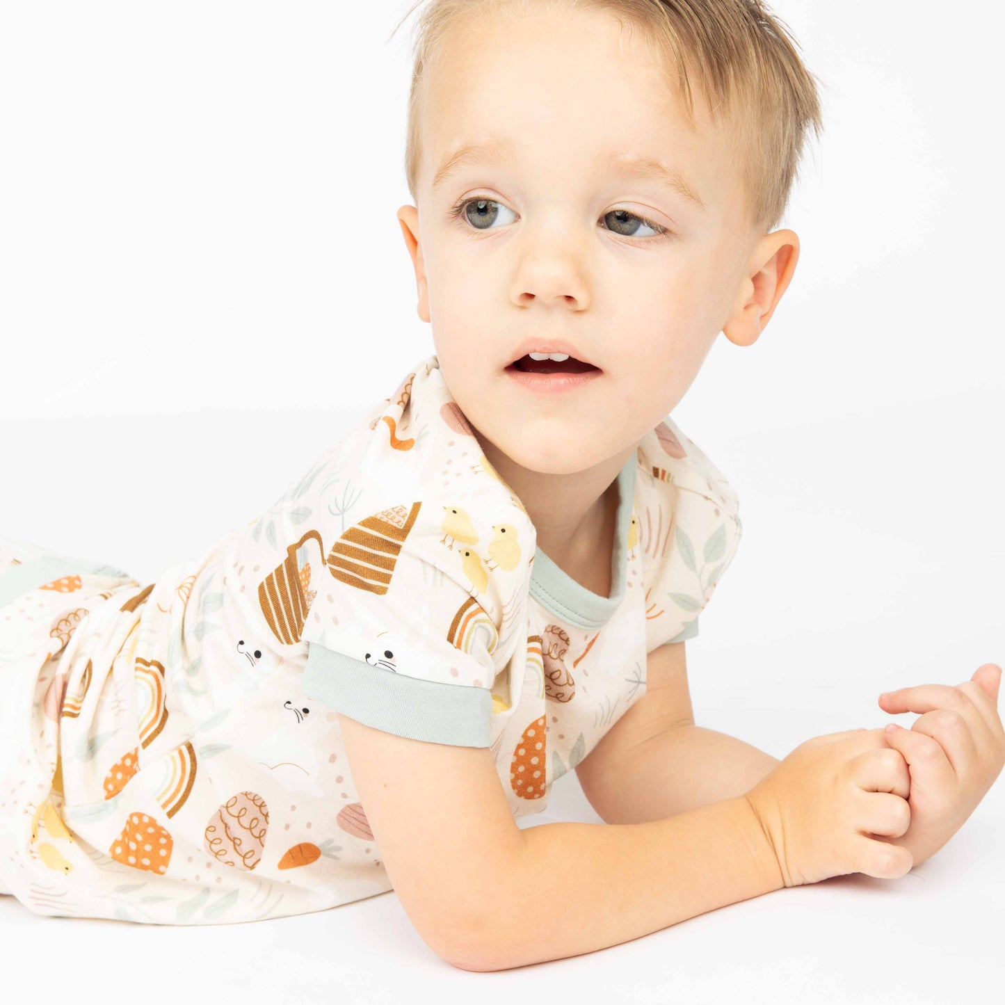 Close up of kid laying on his stomach in his Hop to It print that feature bunnies, easter eggs, chicks and more!
