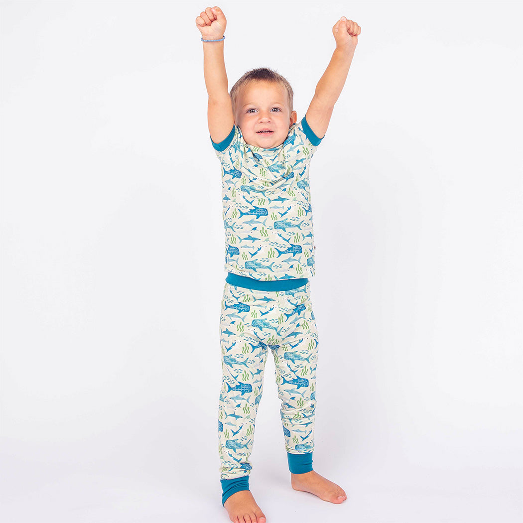 Boy standing with arms up in the air wearing our Shark Friends Two-piece Bamboo Pajamas. 