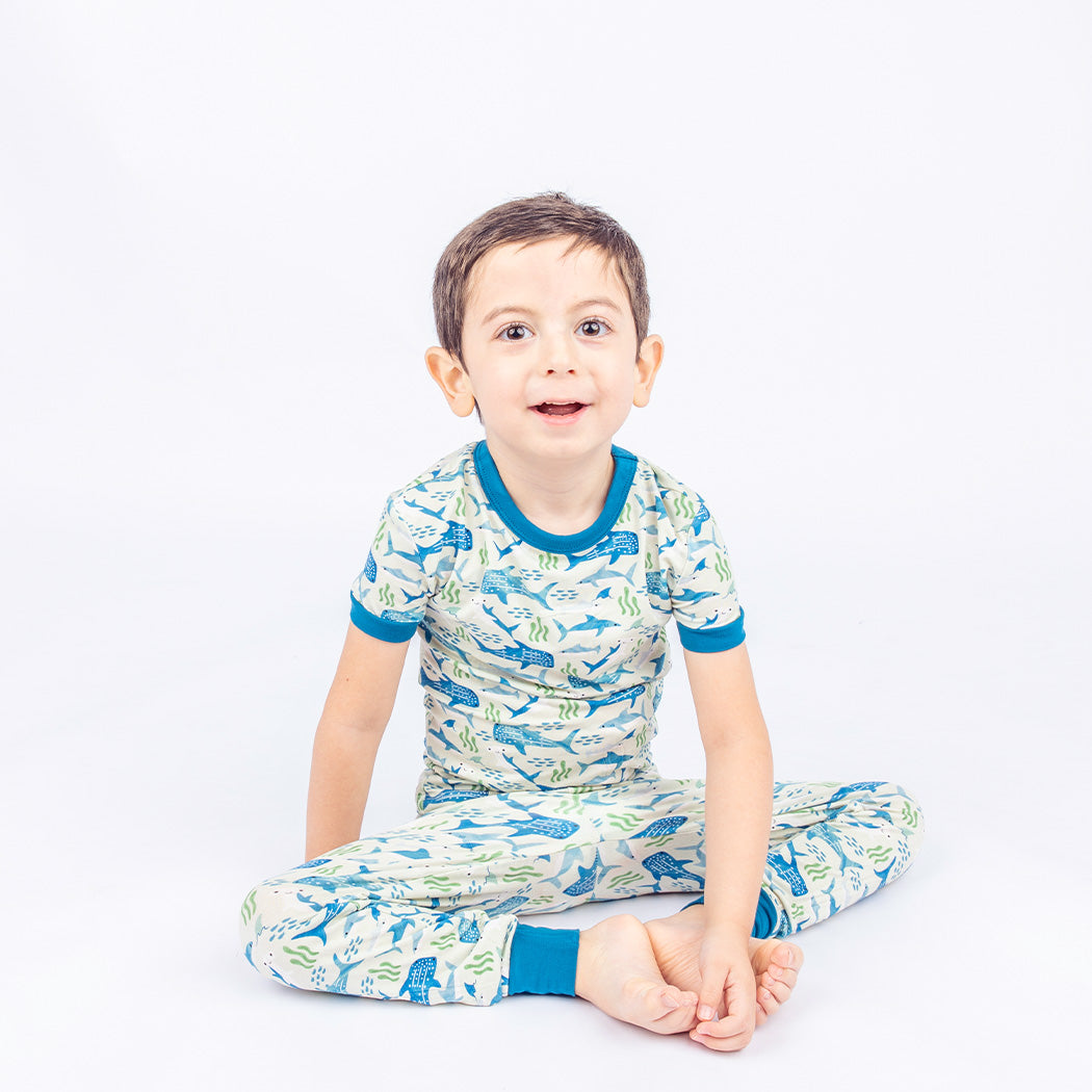 Boy sitting criss cross on the ground, wearing our Shark Friends Two-piece Bamboo Pajamas. 