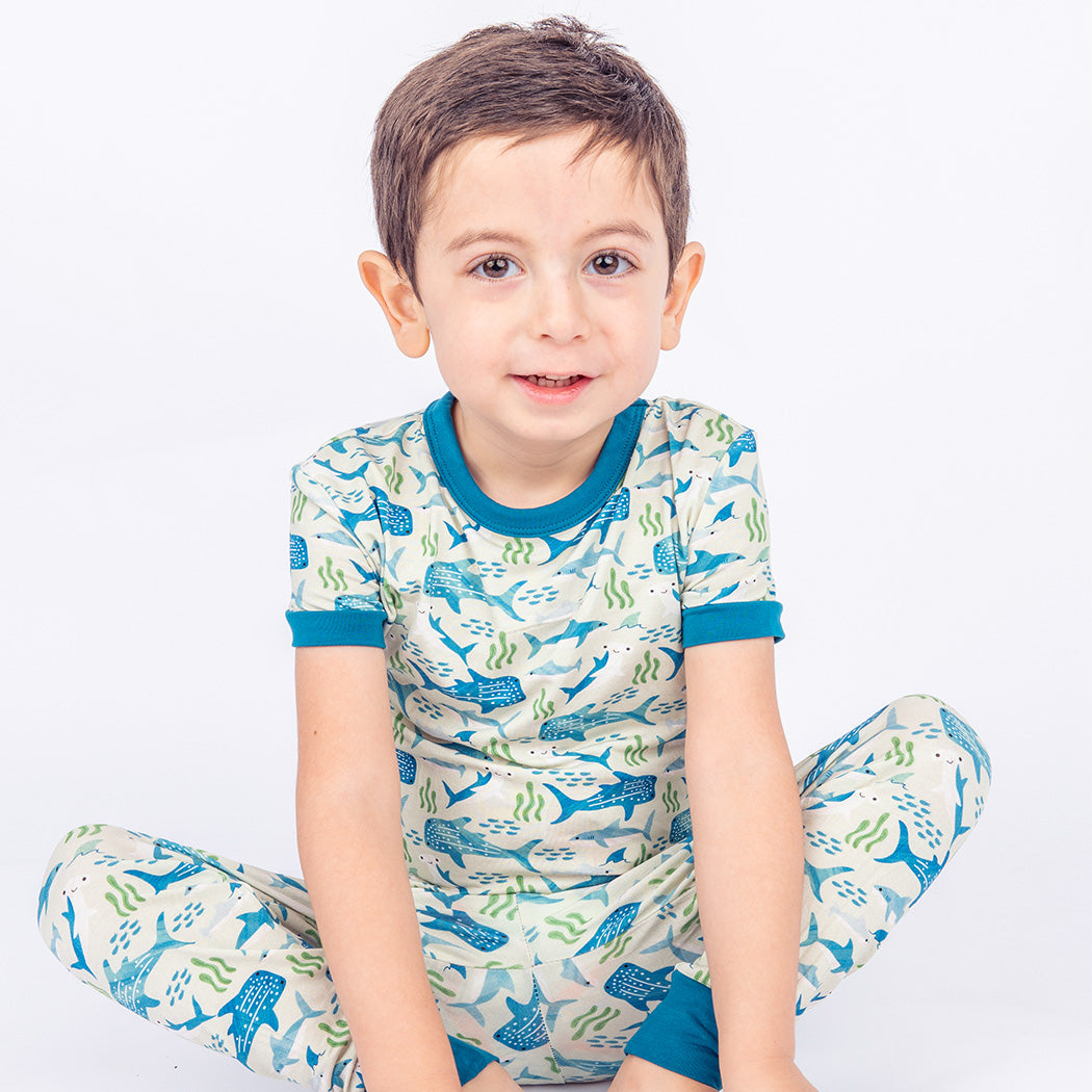 Boy sitting criss cross on the ground, wearing our Shark Friends Two-piece Bamboo Pajamas. 