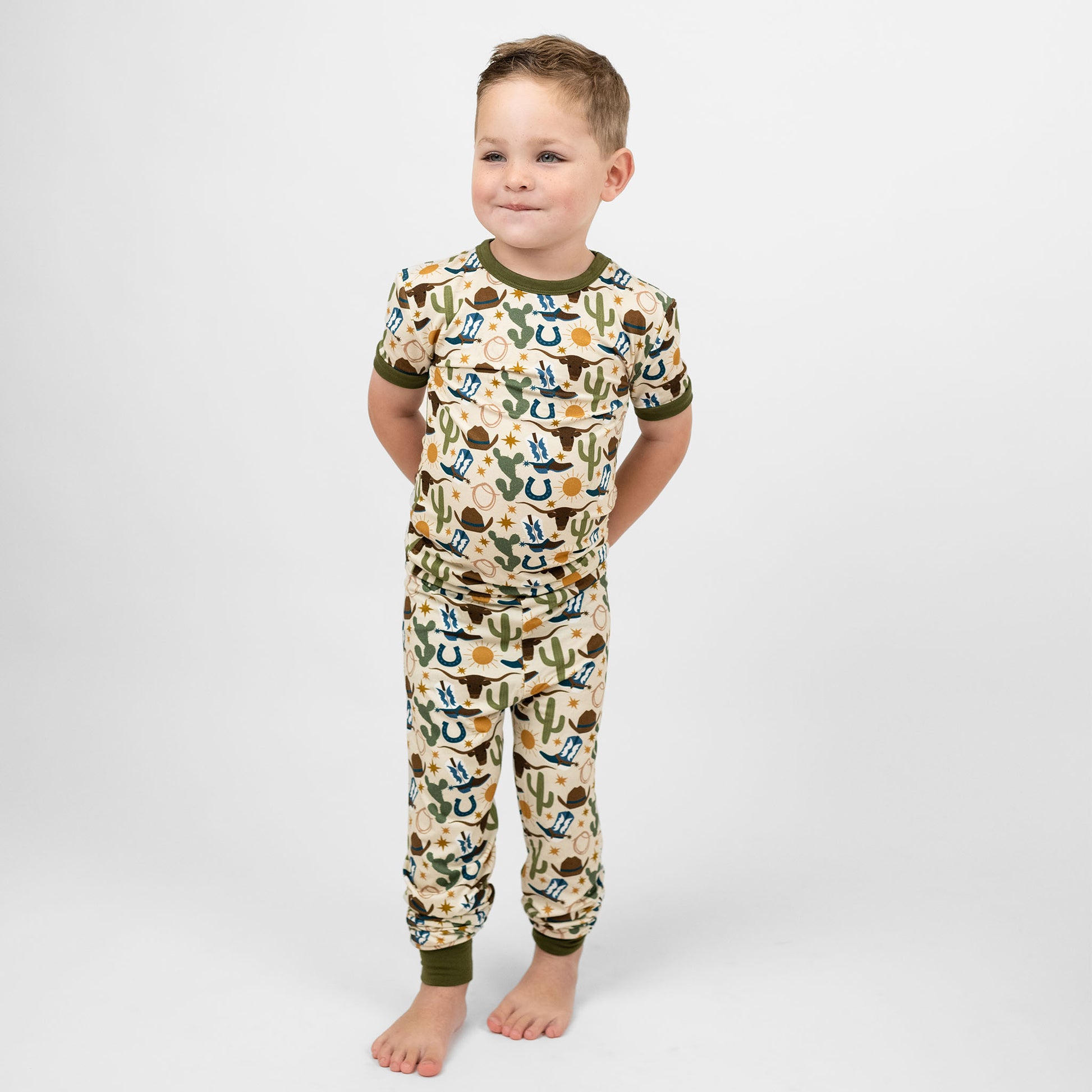 Toddler boy wearing our Western Howdy Collection! This cozy bamboo 2-piece pajama features a charming cowboy-themed print with blue boots, cacti, suns, horseshoes, and cowboy hats. Perfect for western cozy vibes. 