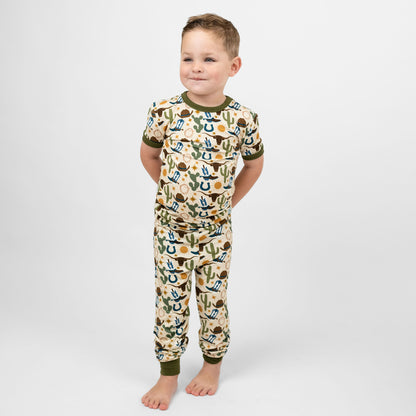 Toddler boy wearing our Western Howdy Collection! This cozy bamboo 2-piece pajama features a charming cowboy-themed print with blue boots, cacti, suns, horseshoes, and cowboy hats. Perfect for western cozy vibes. 