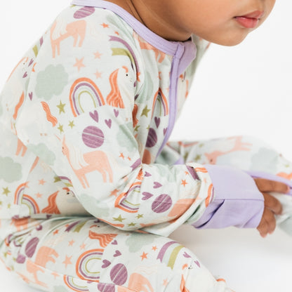 Detailed picture of a baby in our Magical Unicorn bamboo convertible pajama. The print includes unicorns, rainbows, clouds, planets, stars, and hearts. The colors are purple, pink, and blu, with hints of green. 