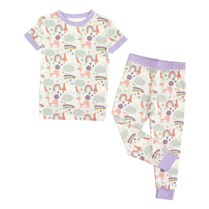 Flat lay image of our Magical Unicorn Toddler Bamboo Pajama. The print includes unicorns, rainbows, clouds, planets, stars, and hearts. The colors are purple, pink, and blu, with hints of green. 