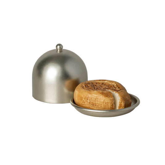 Round loaf of cheese on a metal tray with a dome-shaped lid on a white background