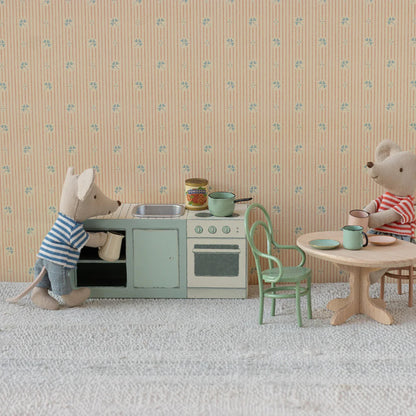 Two toy mice in a miniature kitchen and dining area with floral wallpaper.