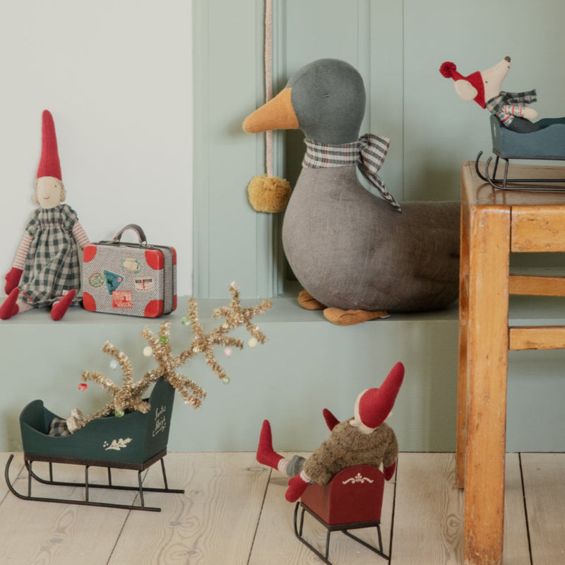 Decorative items including a duck, gnomes, and small sleds on a wooden floor against a light green wall.