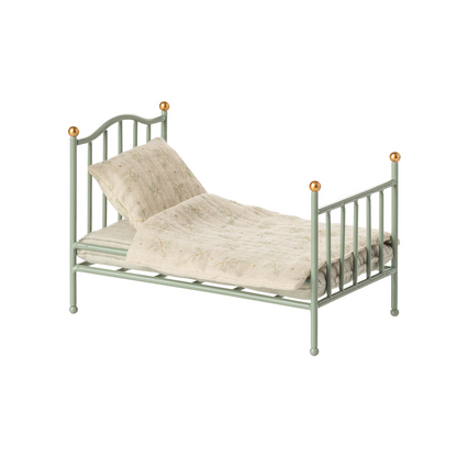 Green metal bed with beige bedding on a white background
