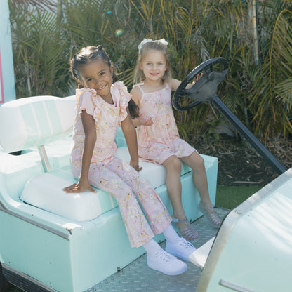 Two young girls in matching outfits sitting in a light blue vehicle with a green outdoor background.