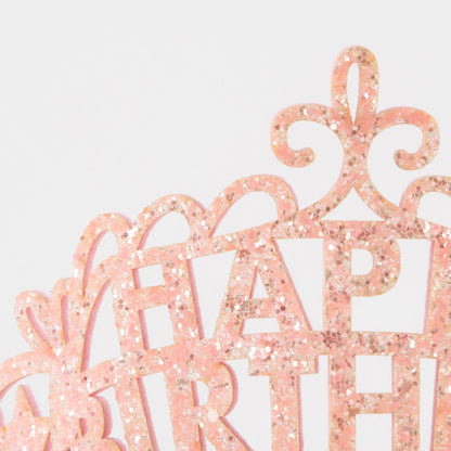 Pink glittery 'Happy Birthday' cake topper on a light gray background